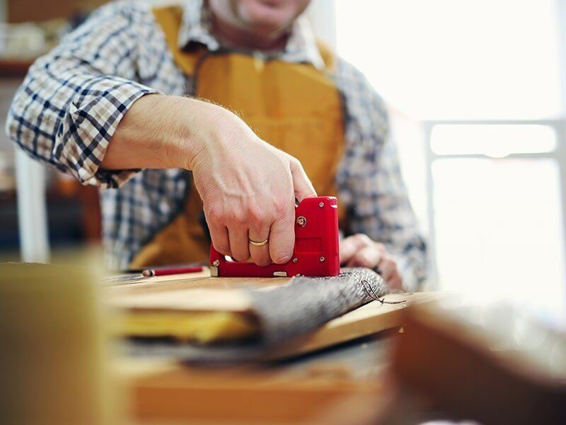 A Man Is Using A Stapler On A Piece Of Wood — Coastal Upholstery In Berkeley Vale, NSW