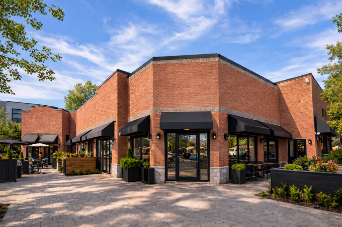 Restaurant en briques avec portes vitrées et terrasse extérieure sous un ciel bleu