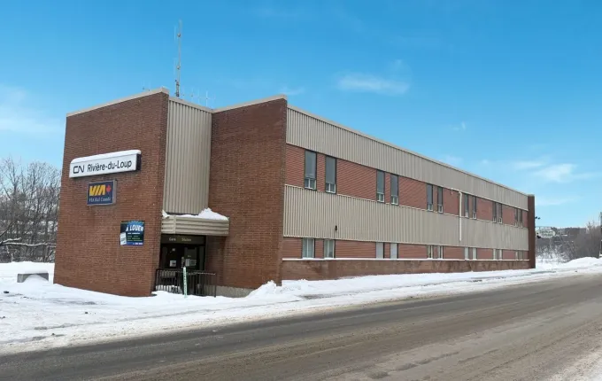 Bâtiment commercial en briques au bord d'une route enneigée sous un ciel bleu clair