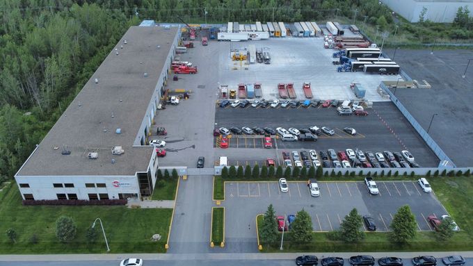 Vue aérienne d'un grand entrepôt et d'un parking avec camions, voitures et quais de chargement.