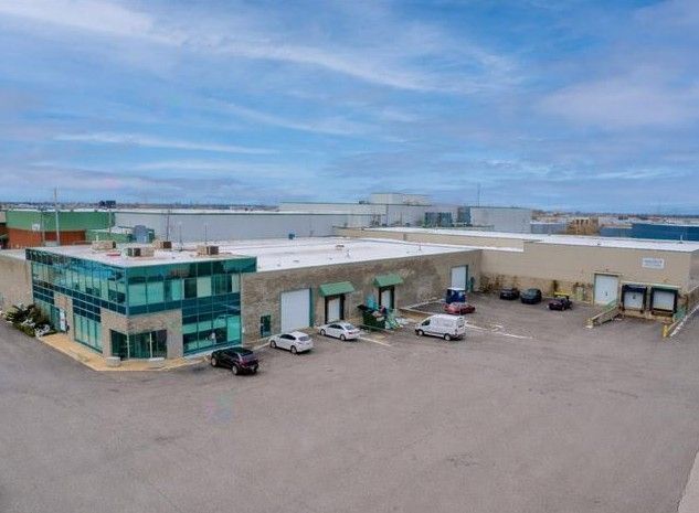 Cour d'entrepôt industriel avec camions et immeuble de bureaux à façade vitrée sous un ciel nuageux
