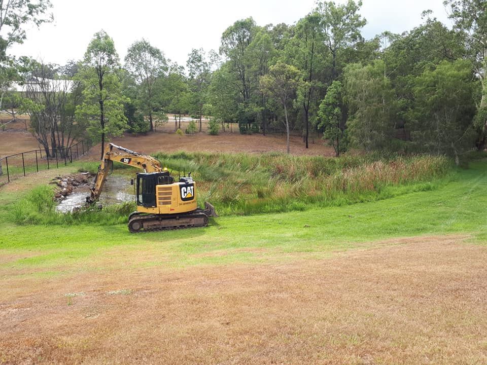 A Large Yellow Excavator Is In The Middle Of A Grassy Field — Dams Cleaned in Sunshine Coast, QLD