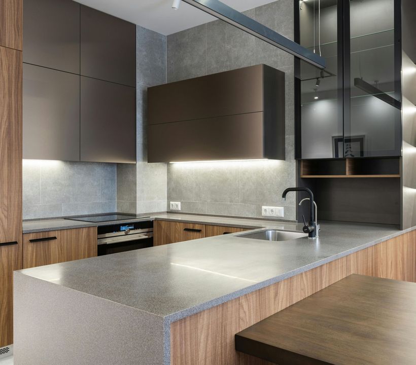 Cuisine moderne avec placards en bois et gris, îlot en pierre, évier, plaque de cuisson et luminaires suspendus.