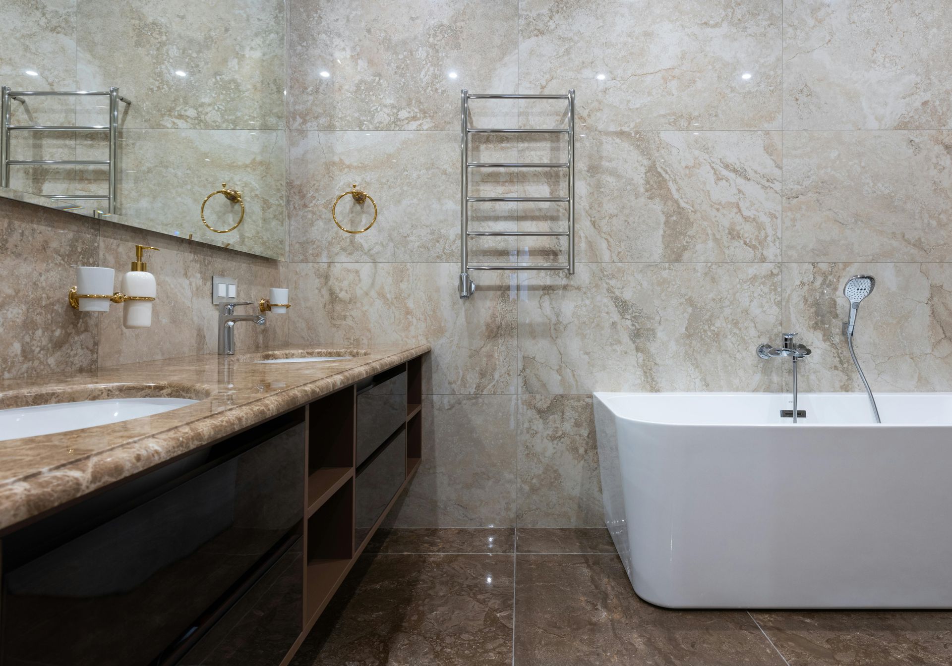 Salle de bains moderne avec murs en marbre, meuble-lavabo foncé, miroirs muraux, porte-serviettes et baignoire blanche sur pieds.