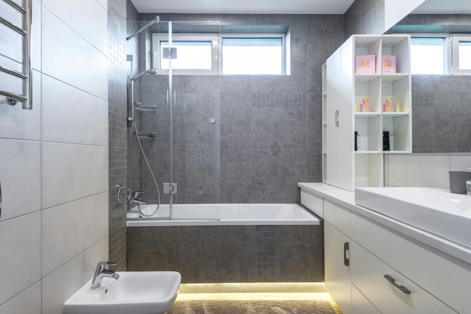 Salle de bains moderne carrelée de gris avec baignoire, douche, lavabo et meuble-lavabo éclairé