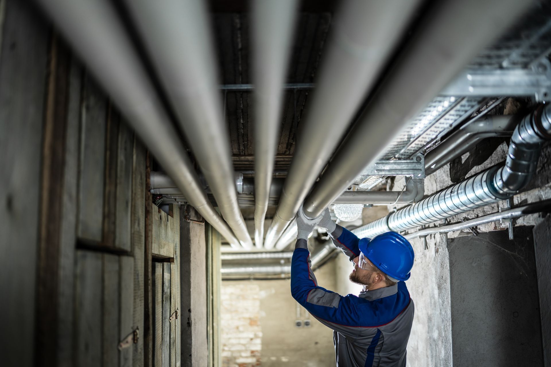 Un technicien portant un casque bleu inspecte les canalisations aériennes d'un tunnel de service industriel.