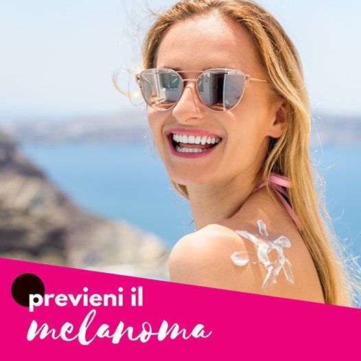 Donna sorridente con occhiali da sole, crema solare applicata a forma di fiore sulla spalla, sfondo spiaggia. Testo: Prevenire il melanoma.