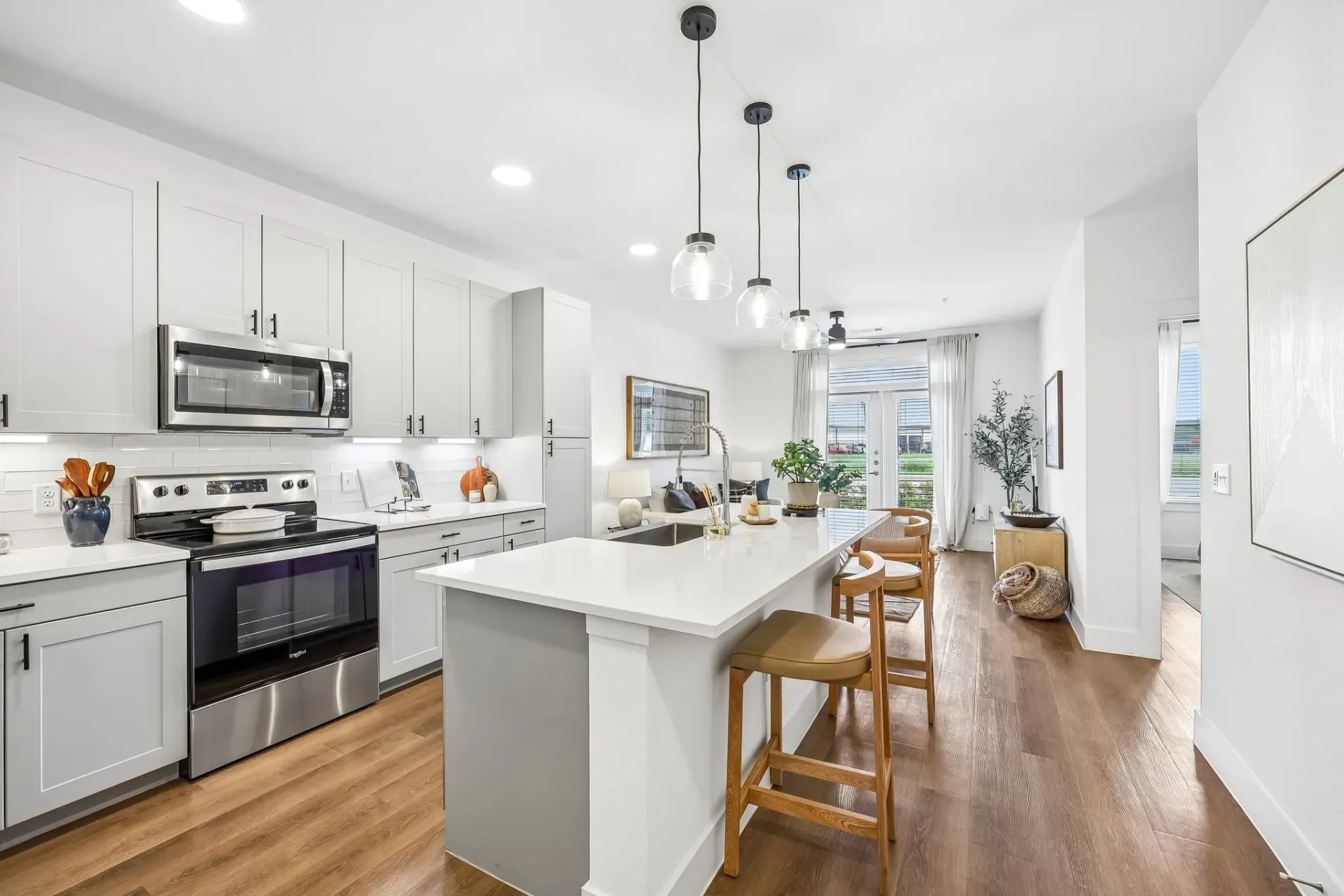 Modern kitchen with a large island and bar stools, overlooking a living area and balcony at The Grayson.