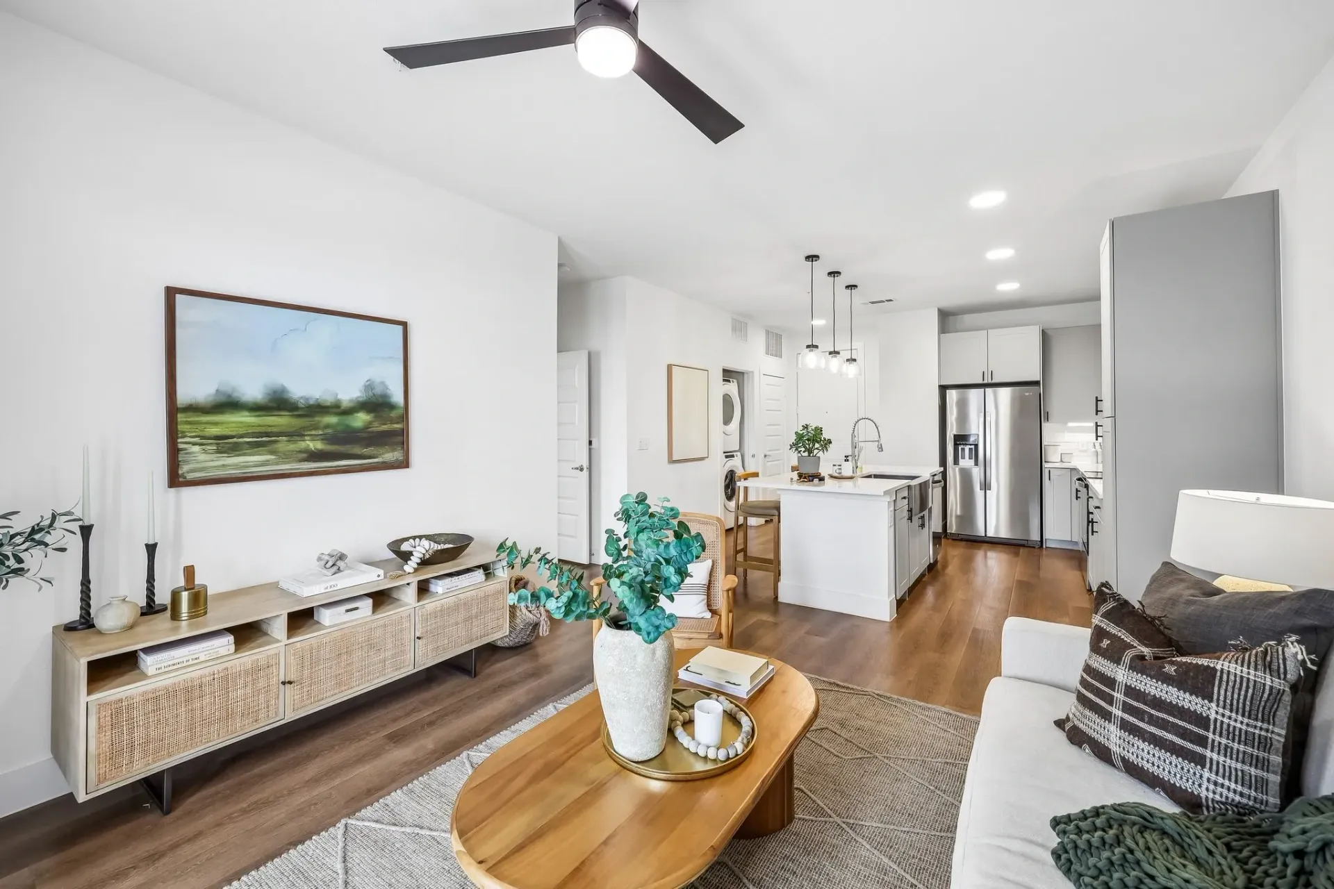 Bright modern living room with white sofa, wood coffee table, patterned rug, and open kitchen in back