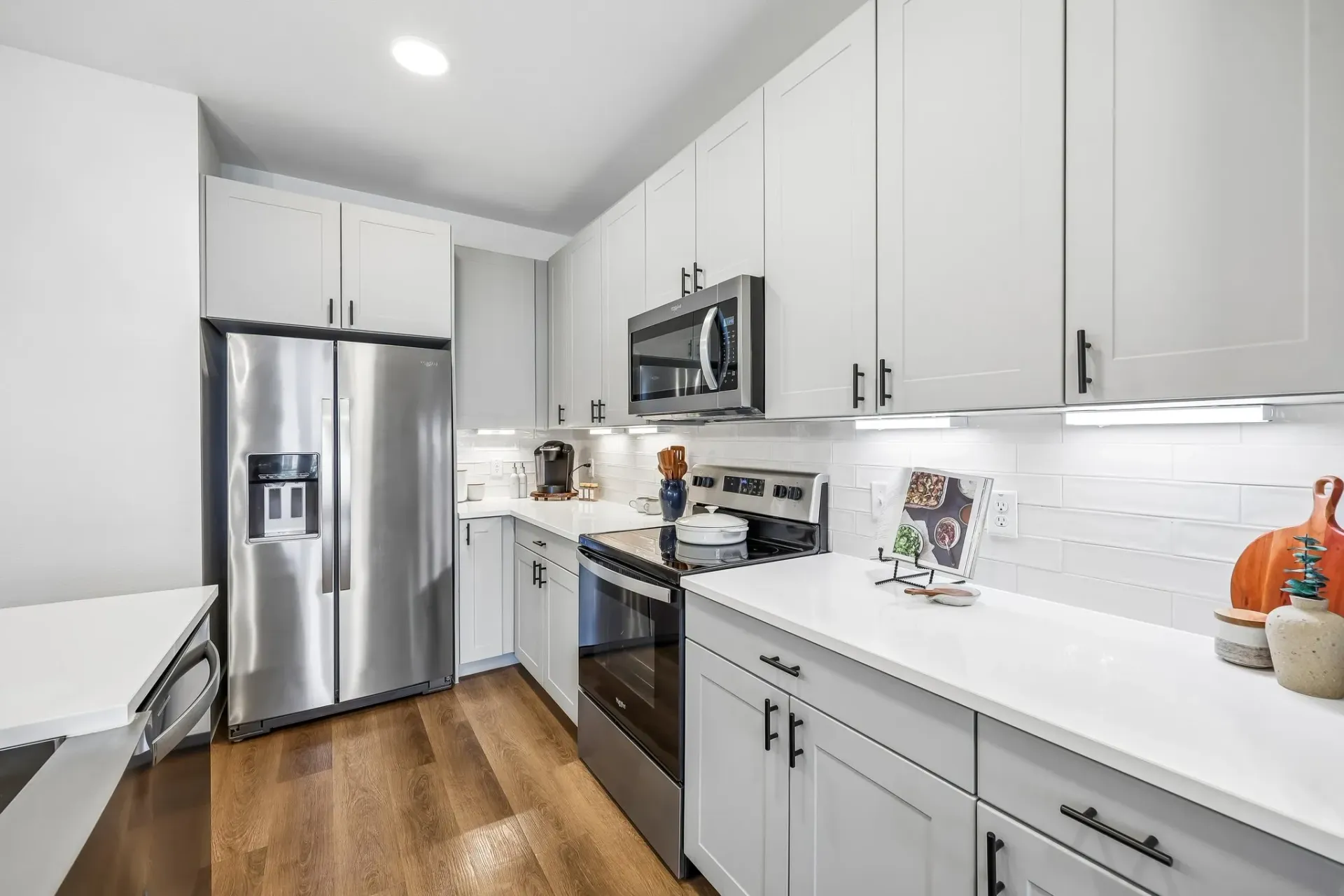 Modern kitchen with stainless steel refrigerator, microwave, and oven. Features white cabinets and subway tile backsplash at The Grayson.