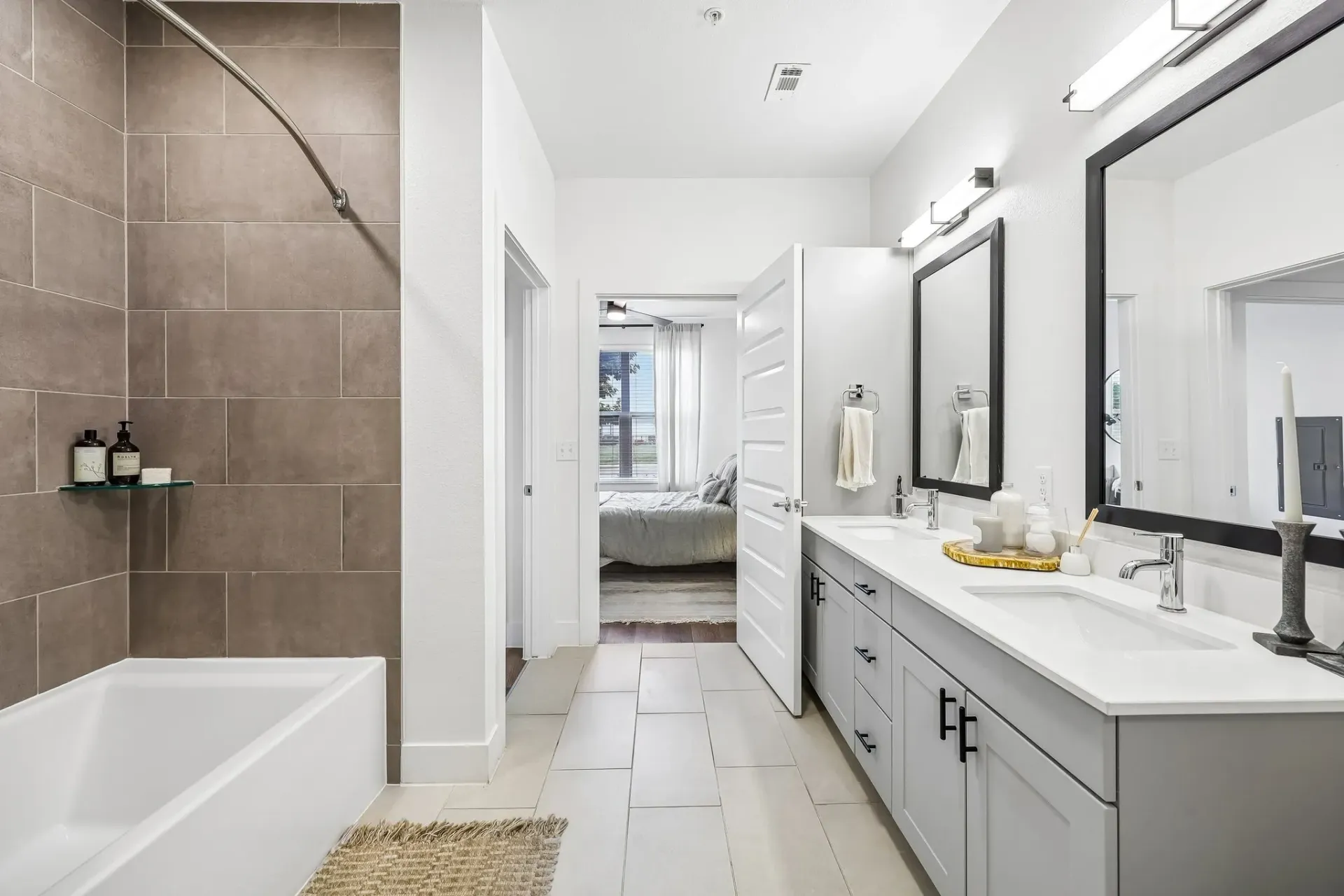 Modern bathroom with double vanity and large mirror, separate tub and shower, and view into bedroom at The Grayson.