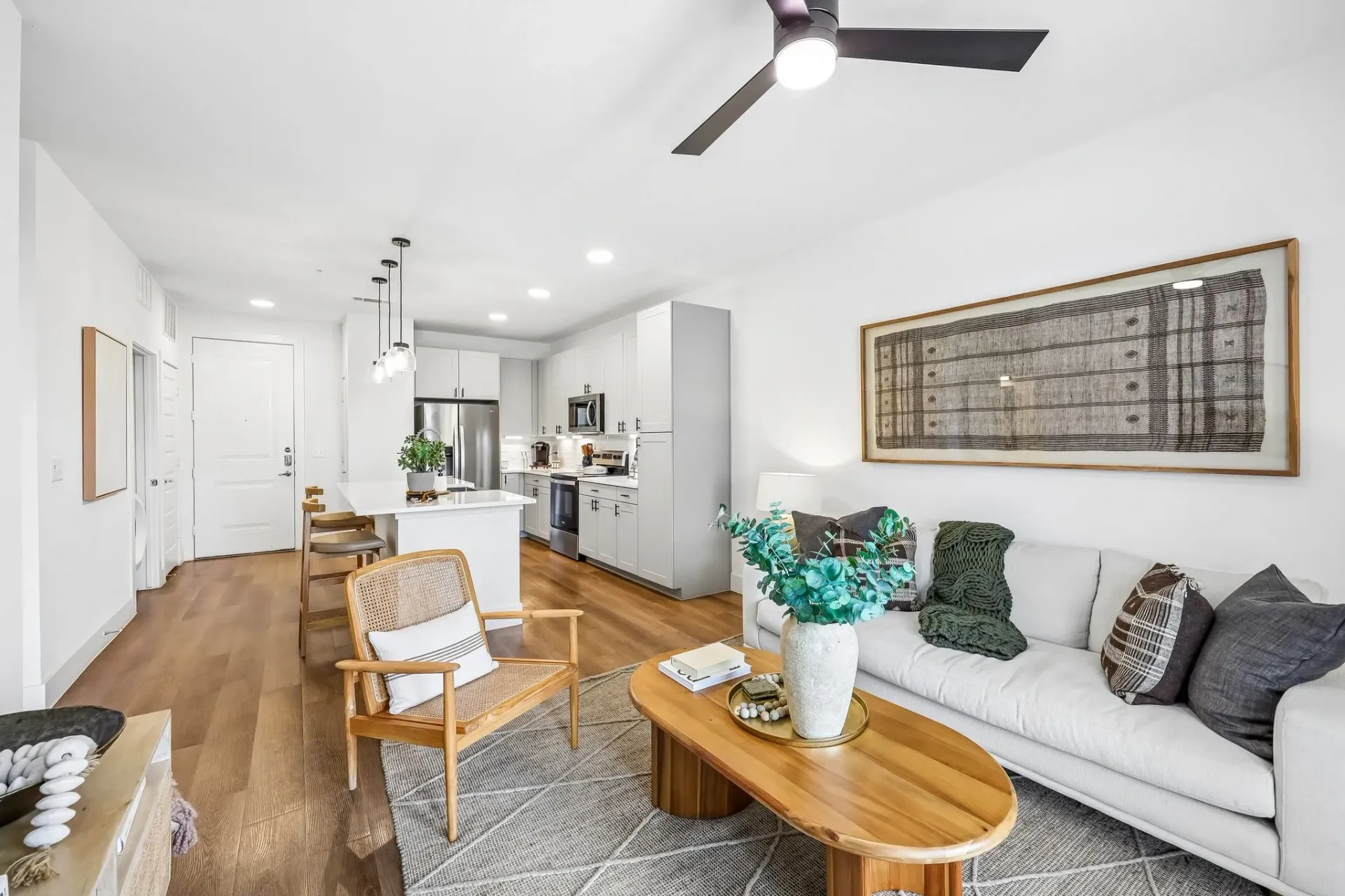 Modern living room and kitchen with white furniture, wood accents, and natural light at The Grayson.