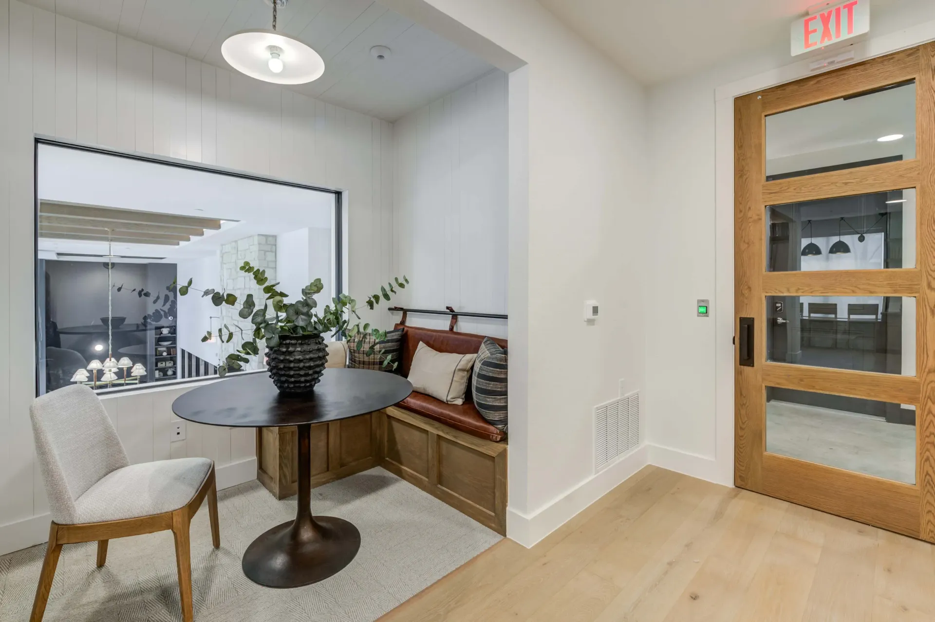 A cozy nook with a round table, chair, and built-in banquette seating, next to a wooden door with glass panels at The Grayson apartments in Fort Worth, TX..
