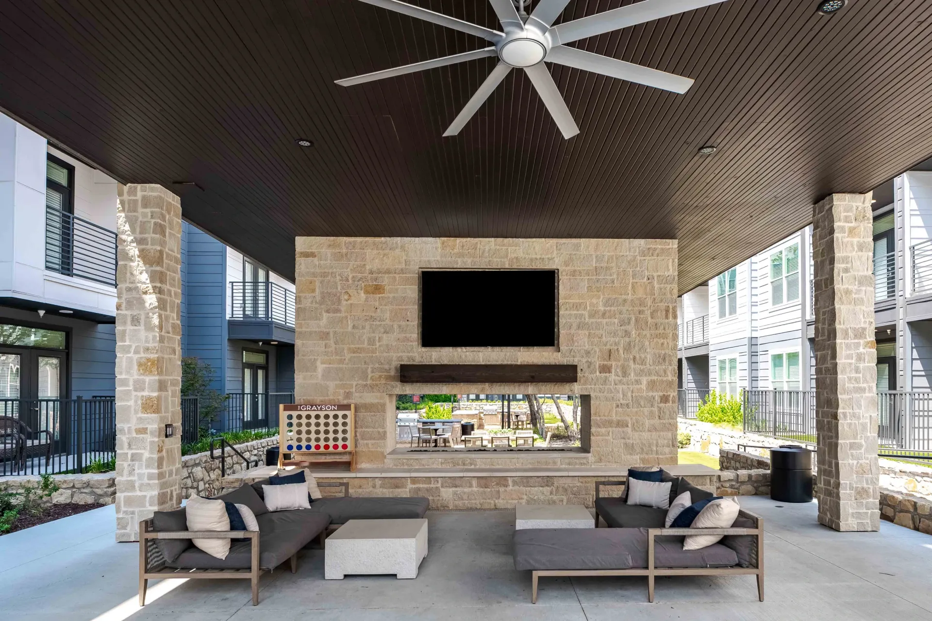 Outdoor lounge area with a large TV, fireplace, and seating, overlooking a courtyard at The Grayson in Fort Worth, TX.