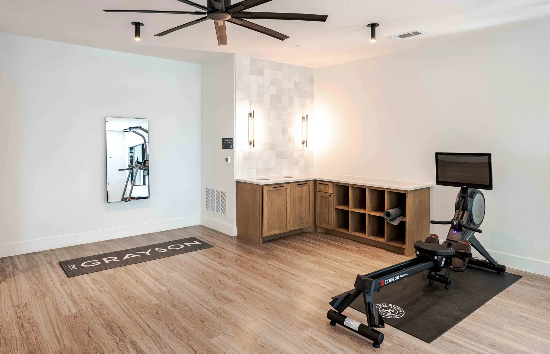 Fitness room with rowing machine, mirror, and workout equipment at The Grayson apartments in Fort Worth, TX..