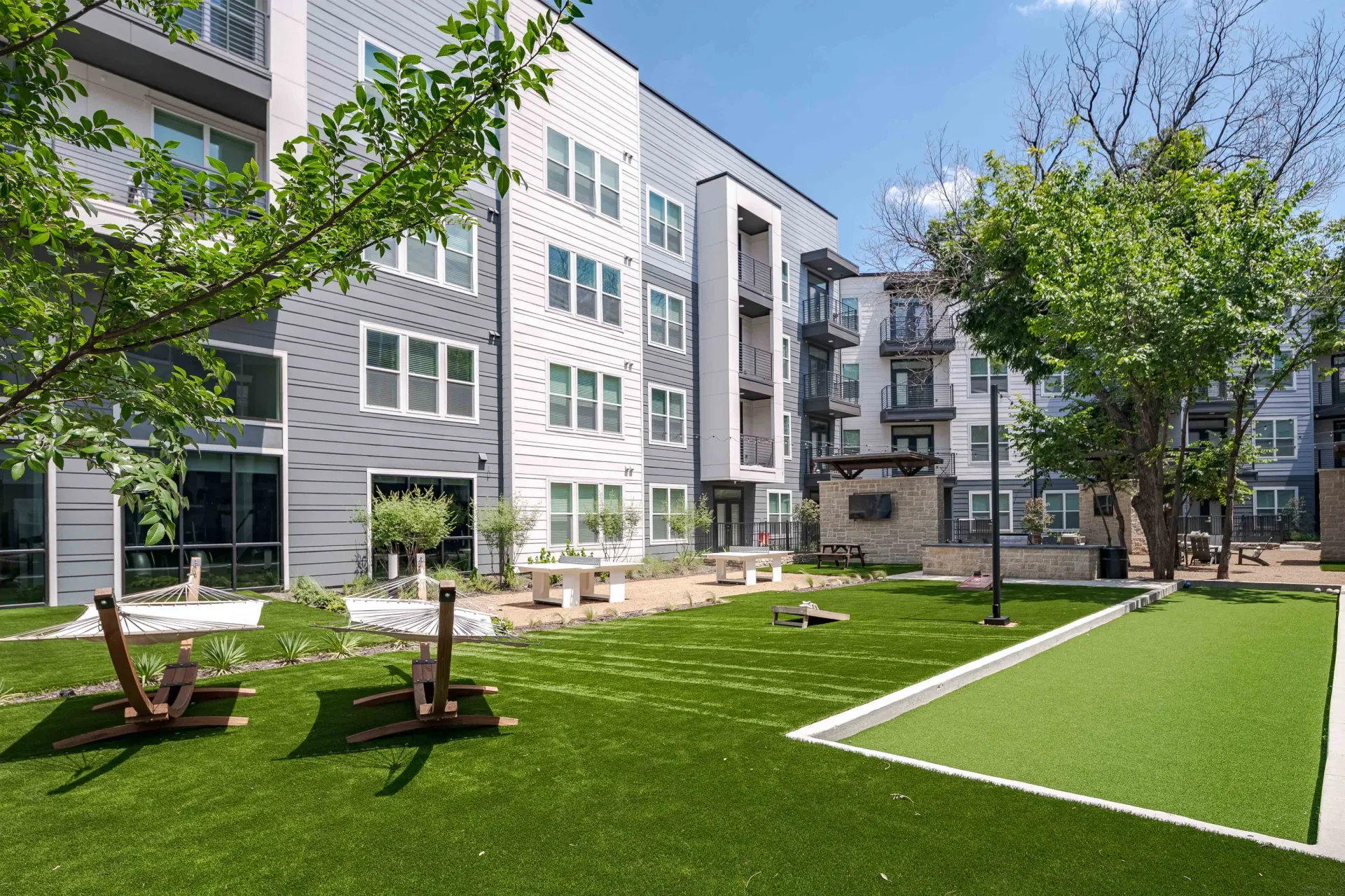 Modern apartment building courtyard with artificial turf, bocce ball court, hammocks, and picnic tables at The Grayson in Fort Worth, TX. 