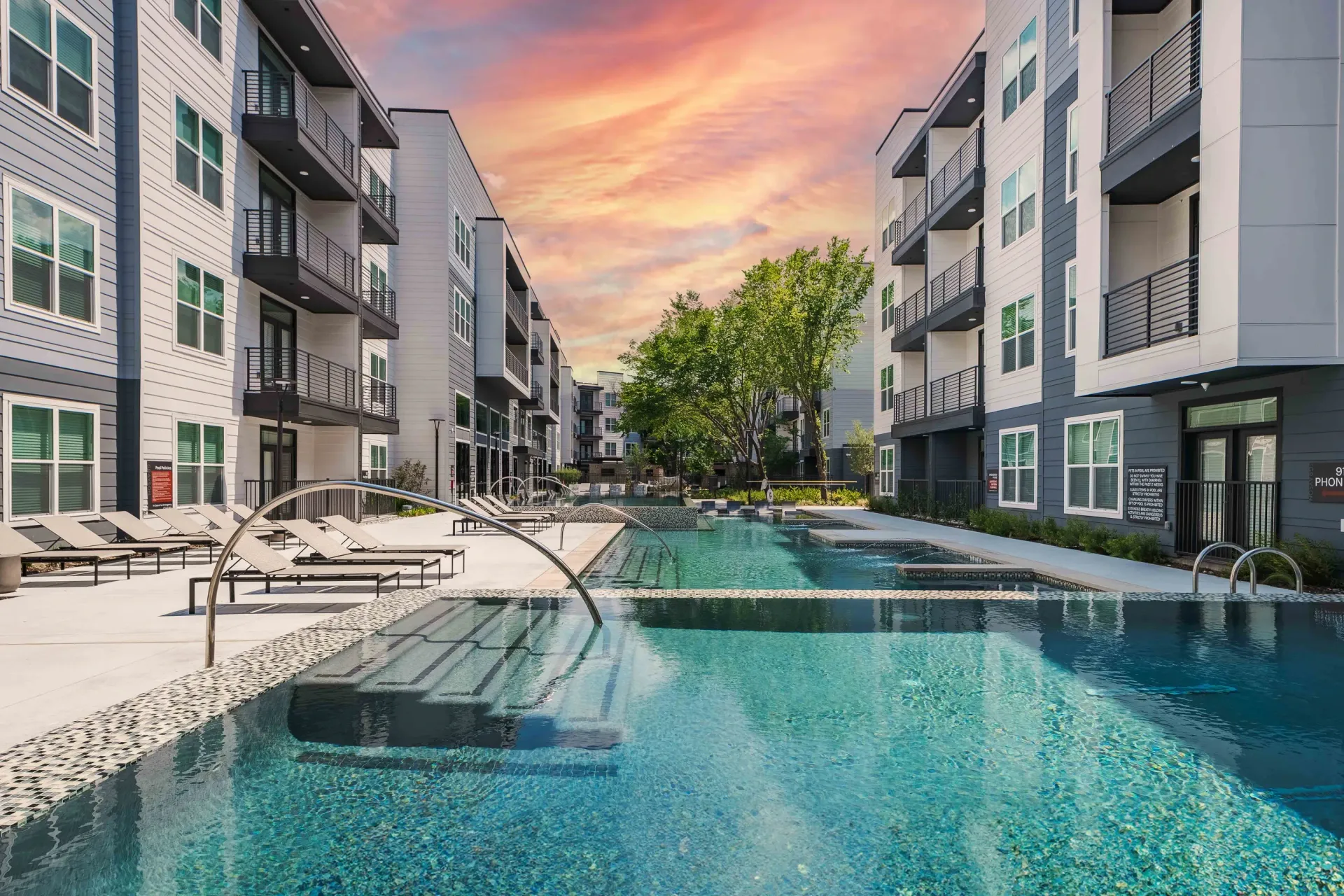 Luxury swimming pool and lounge area between apartment buildings at sunset at The Grayson in Fort Worth, TX.