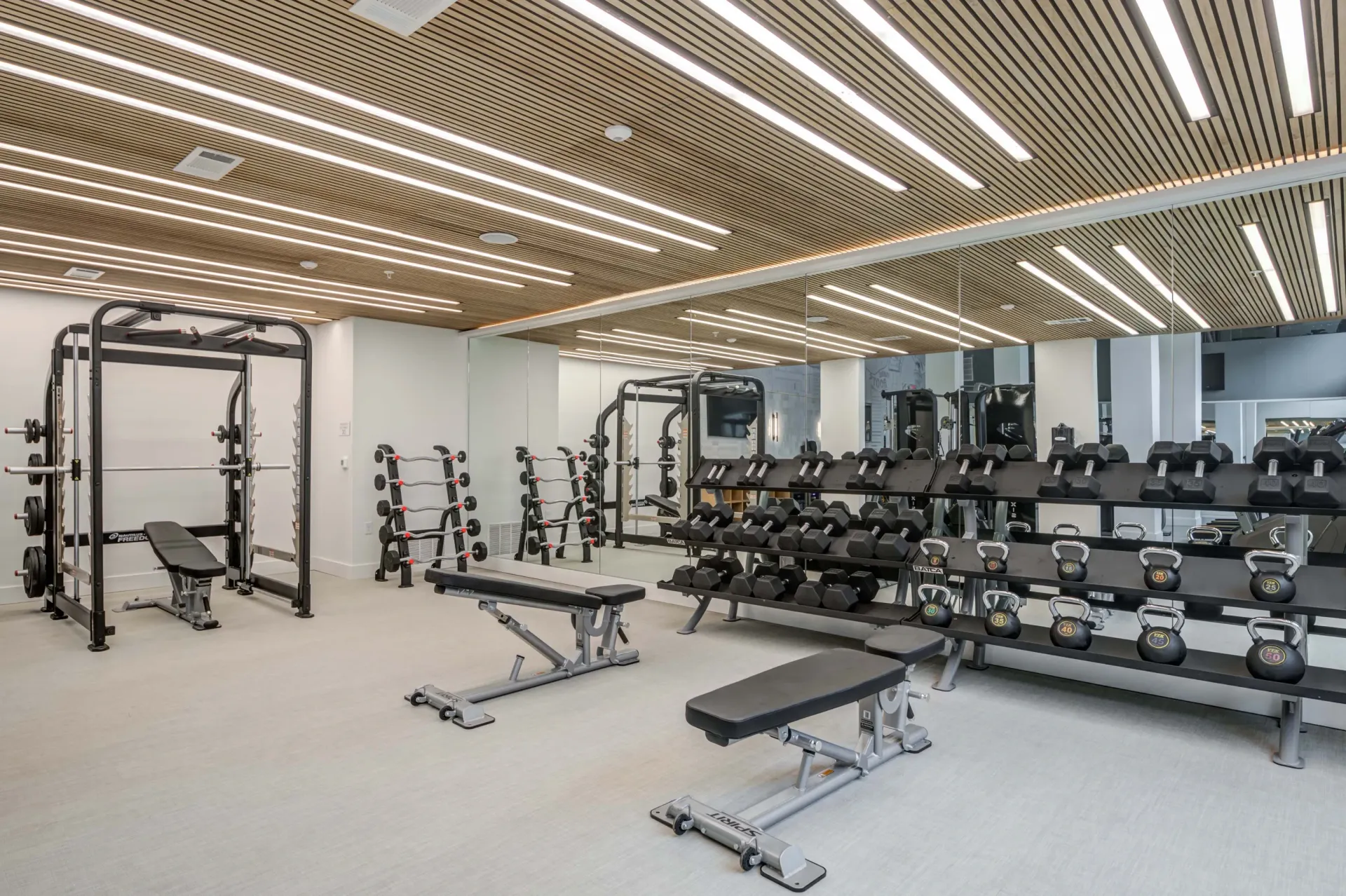 A spacious, well-equipped fitness center with a smith machine, weight racks, dumbbells, kettlebells, and benches at The Grayson apartments in Fort Worth, TX..