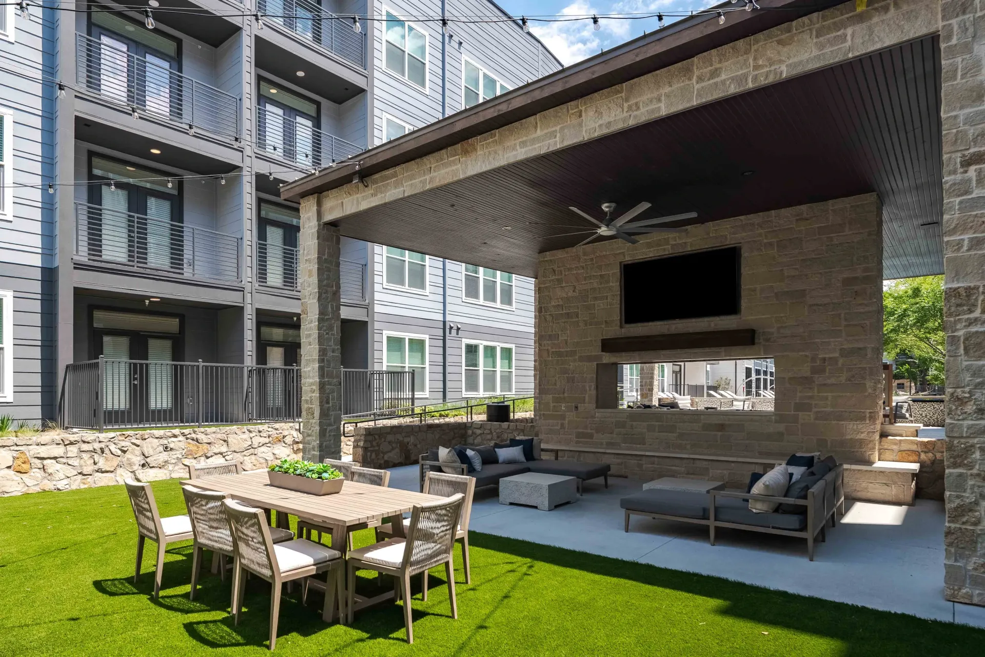 Outdoor lounge area with dining table, seating, fireplace, and TV, adjacent to apartment building at The Grayson in Fort Worth, TX.