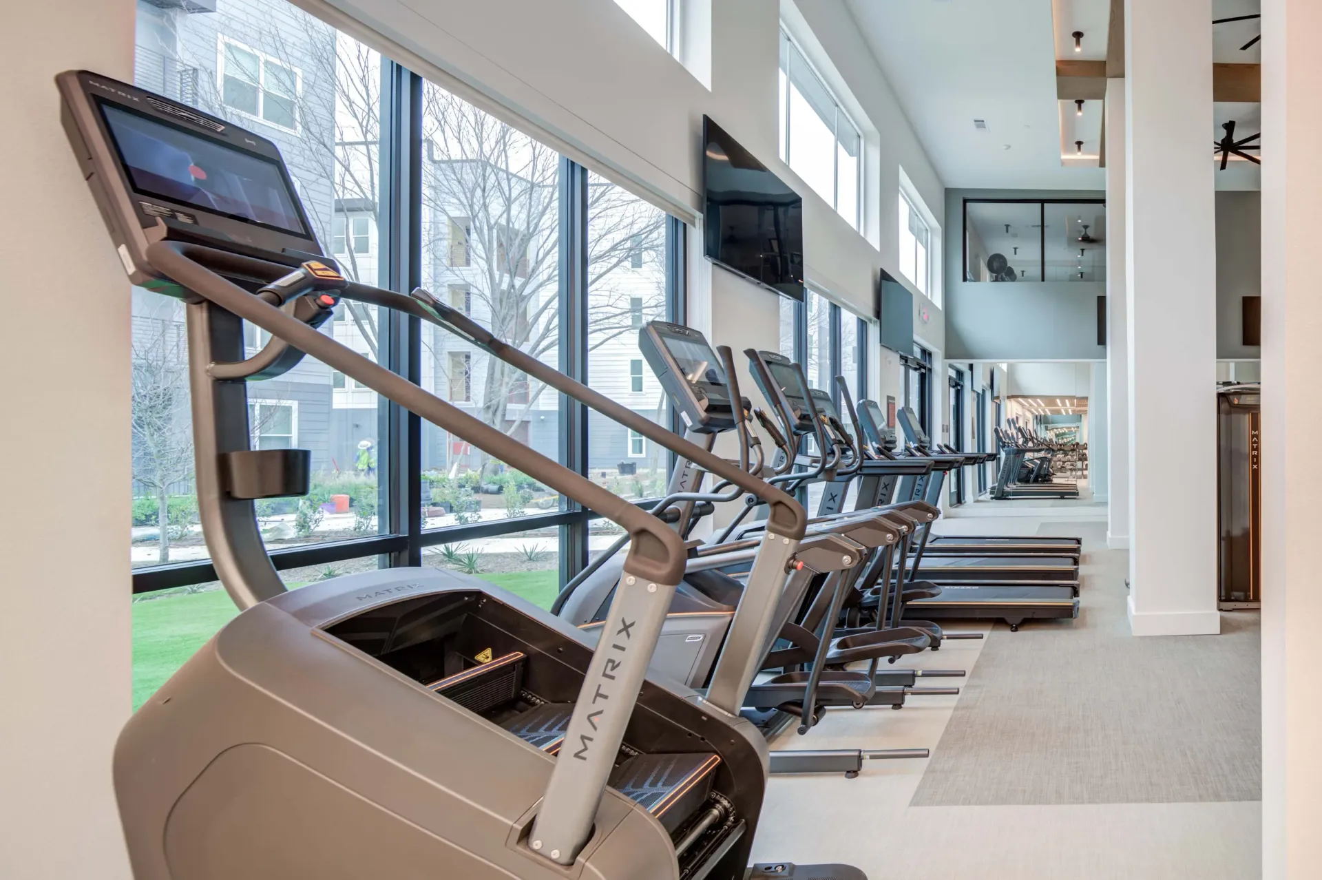 Modern apartment gym with treadmills and stair climbers and large windows at The Grayson apartments in Fort Worth, TX..