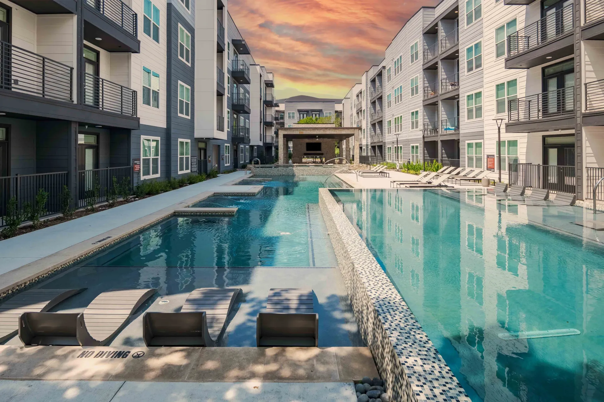 Modern apartment courtyard with a long turquoise swimming pool at sunset at The Grayson in Fort Worth, TX.
