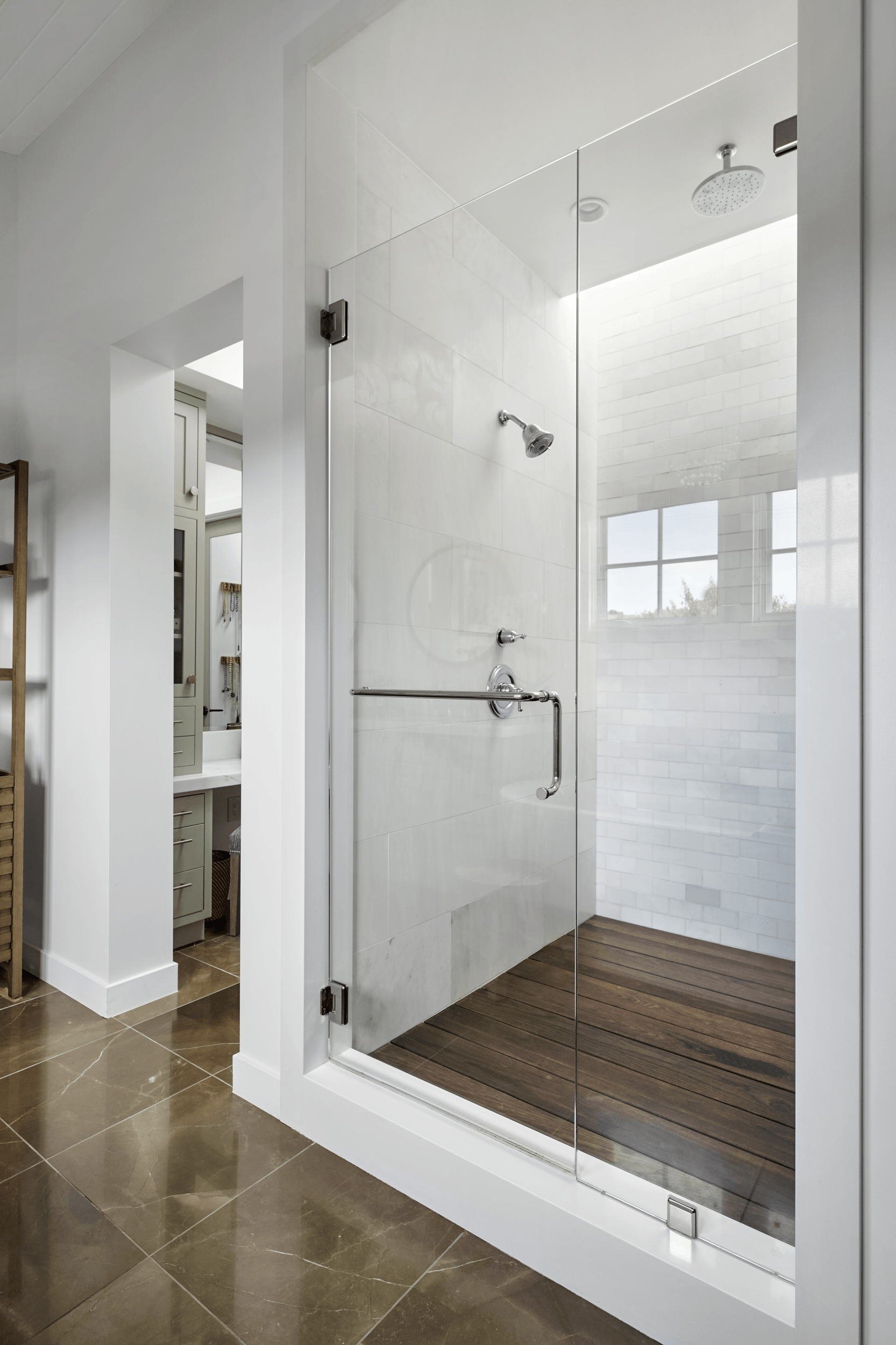A bathroom with a walk in shower with a glass door and a wooden floor.