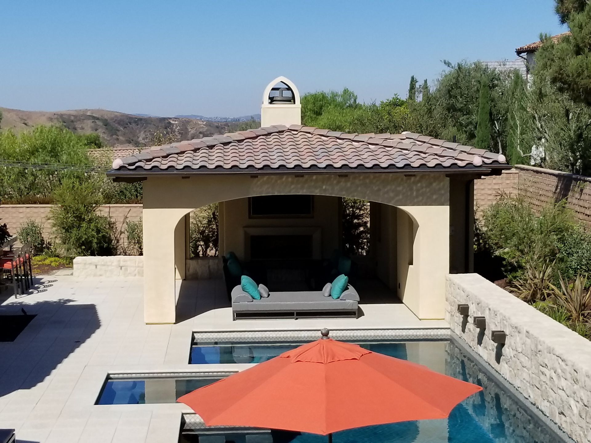 A large umbrella sits in front of a gazebo overlooking a swimming pool