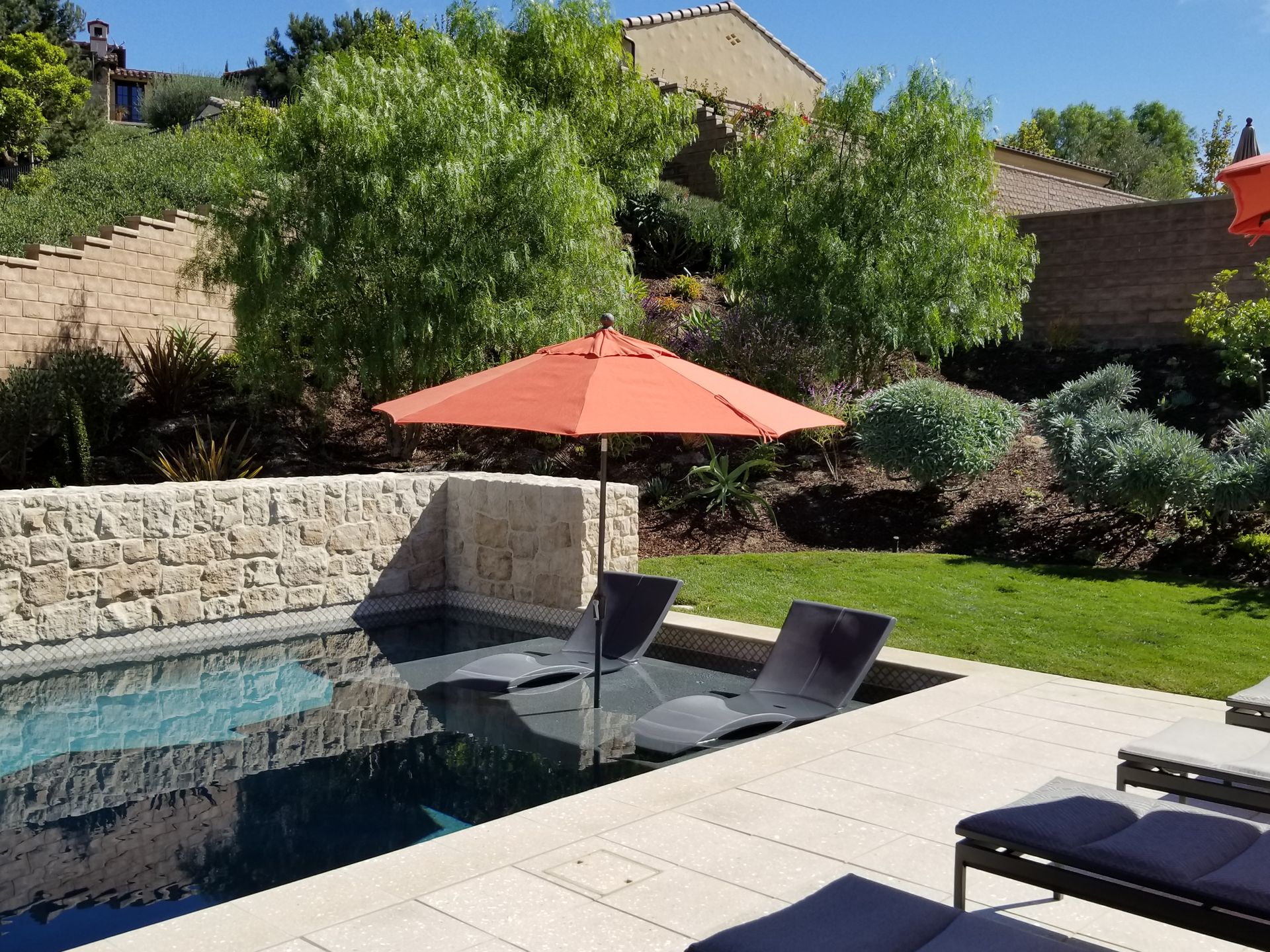 A swimming pool with chairs and an orange umbrella