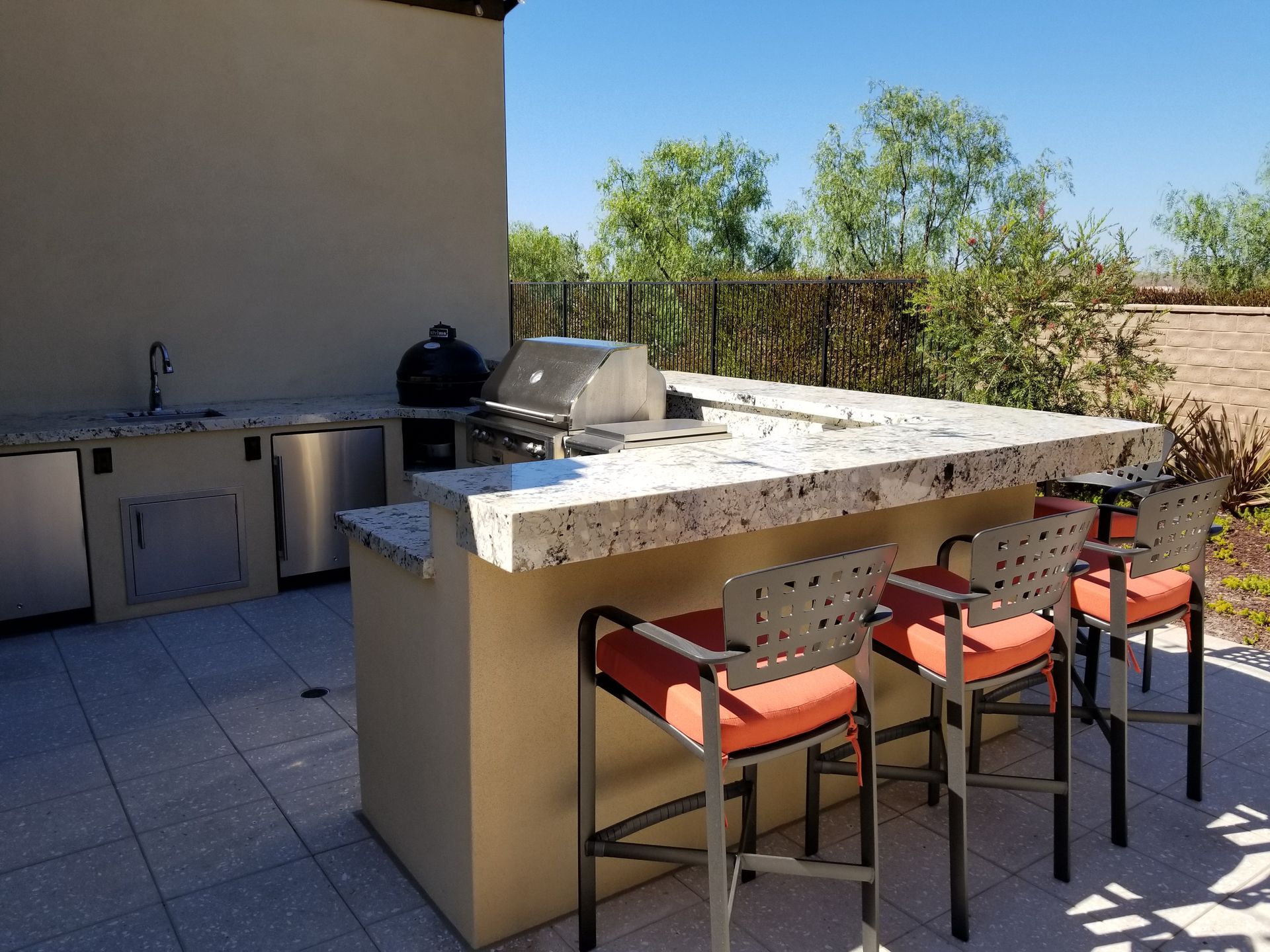 A large outdoor kitchen with a grill and stools