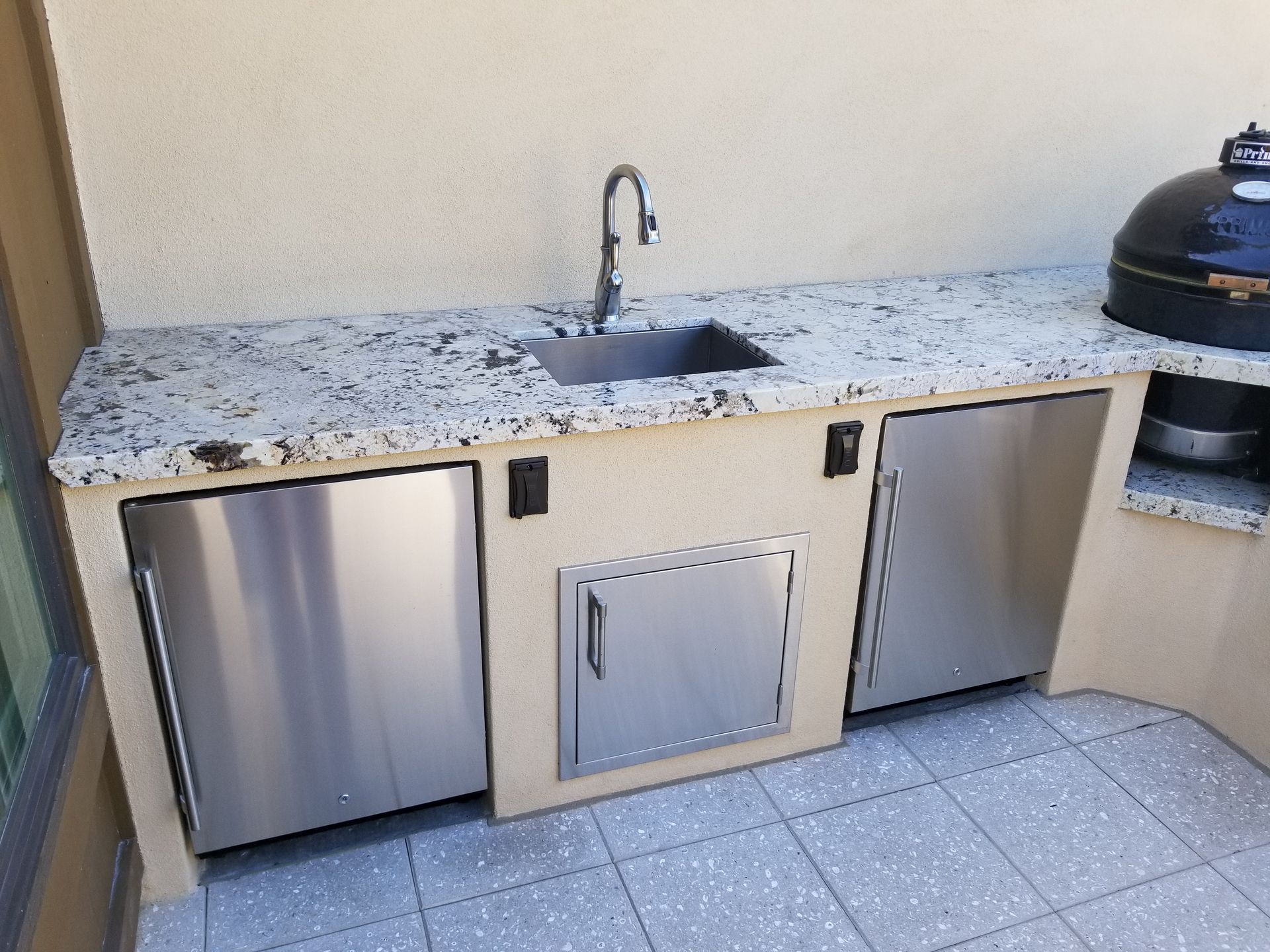 A kitchen with a sink , refrigerator , and grill.