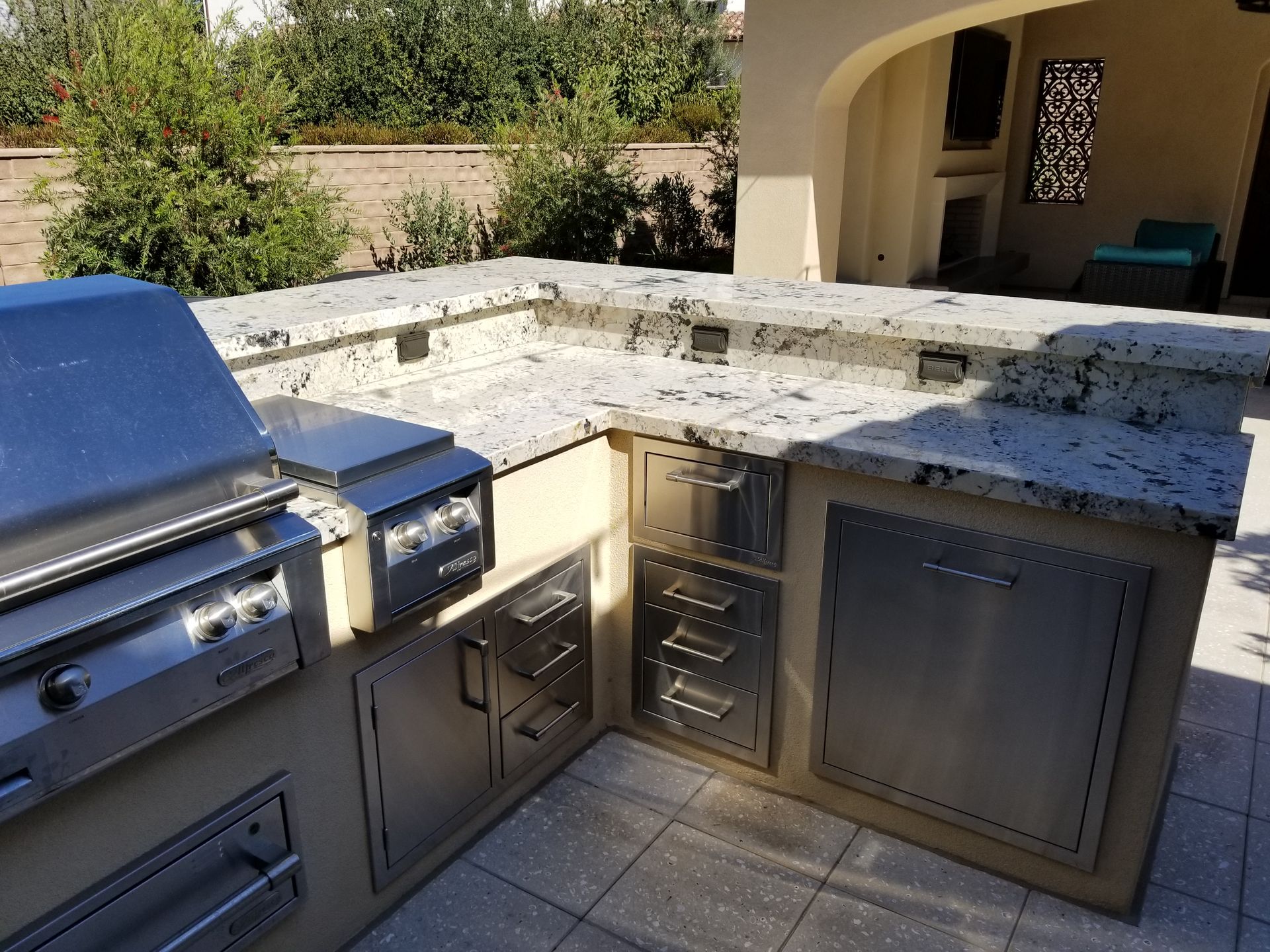 An outdoor kitchen with a grill and granite counter tops