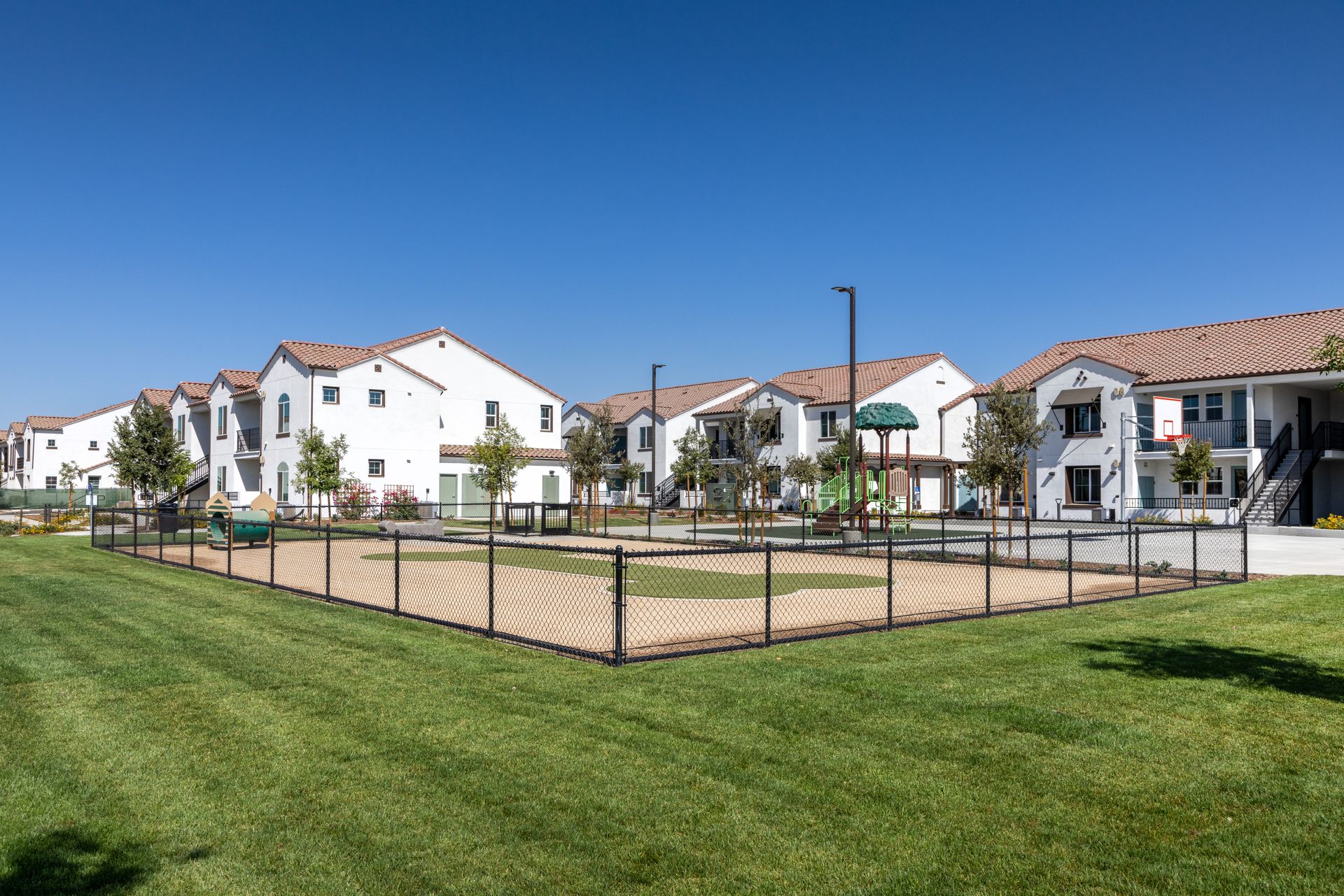 A fenced in dog park in front of a row of apartment buildings.