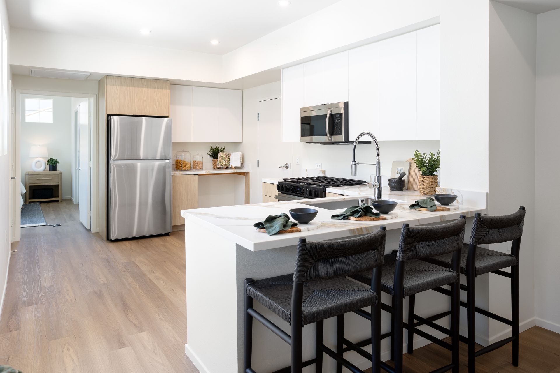 A kitchen with a stainless steel refrigerator , microwave , sink and bar stools.