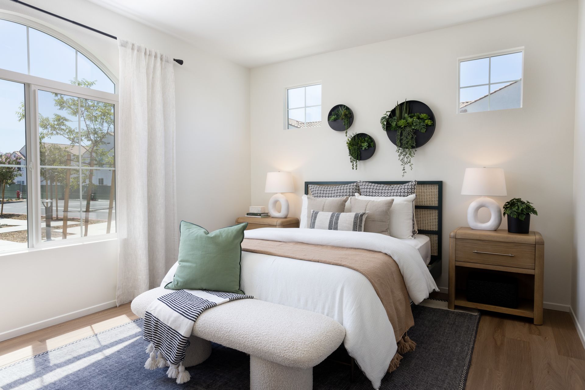 A bedroom with a bed , nightstand , lamps and a bench.