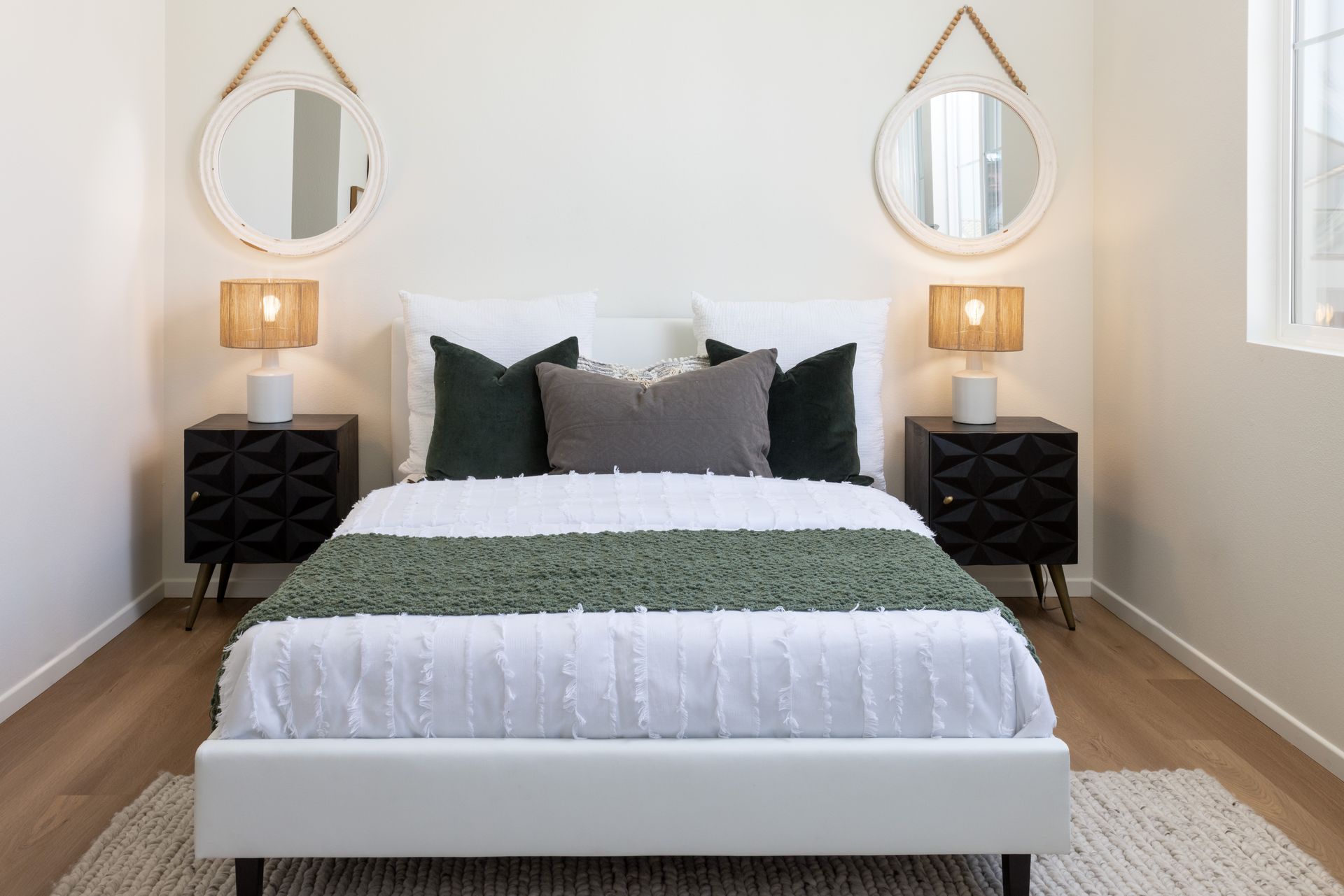 A bedroom with a bed , two nightstands , two mirrors and two lamps.