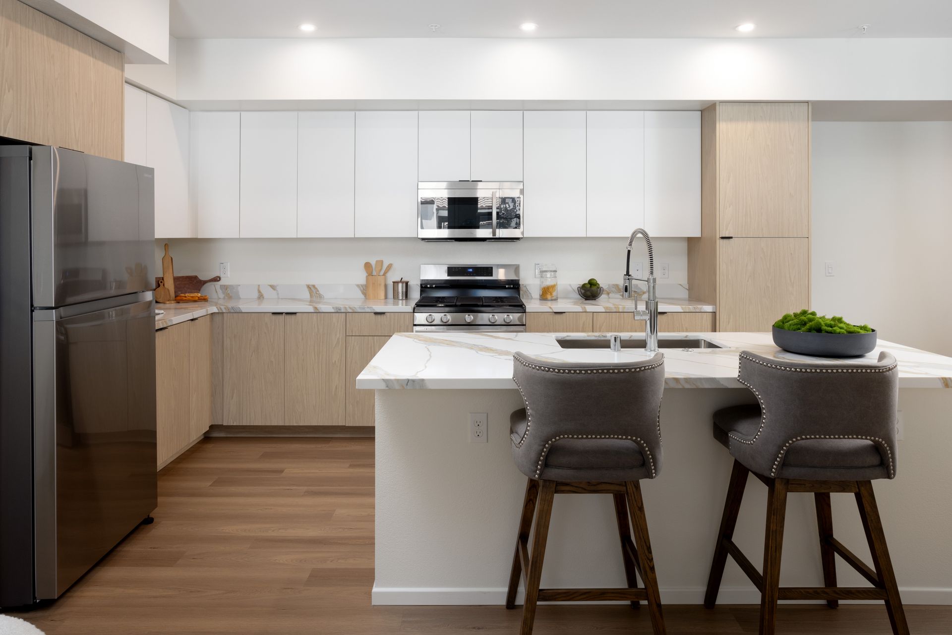 A kitchen with white cabinets , stainless steel appliances , a refrigerator and a sink.