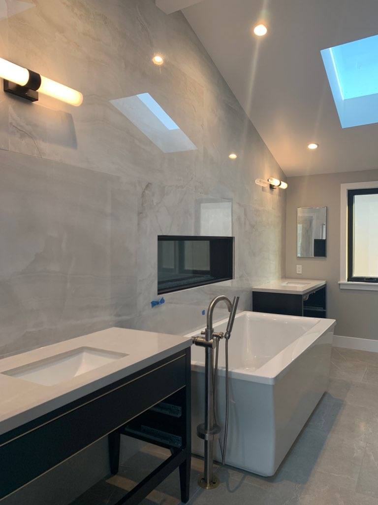 A bathroom with a tub , sink , mirror and skylight.