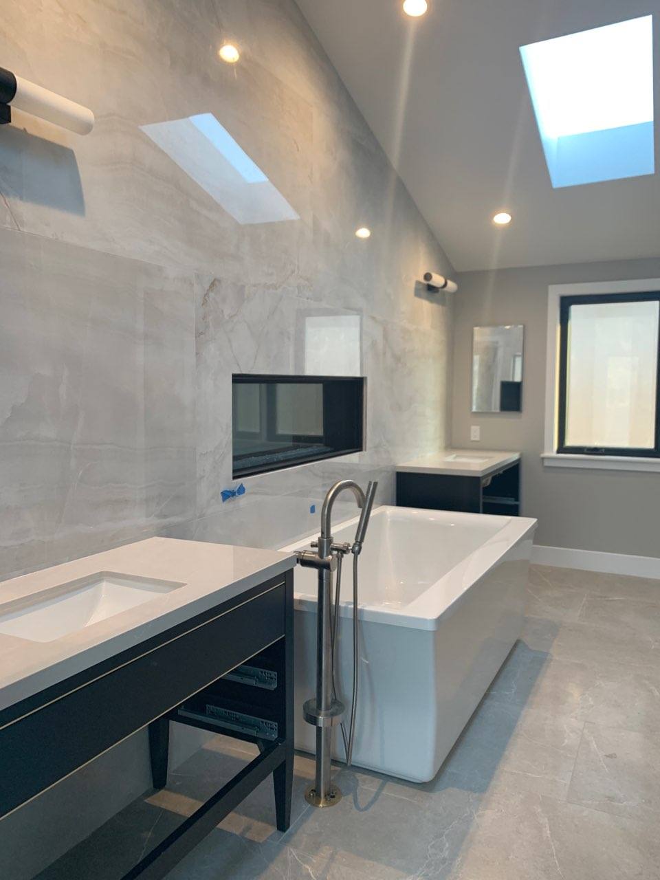 A bathroom with a tub , sink , mirror and skylight