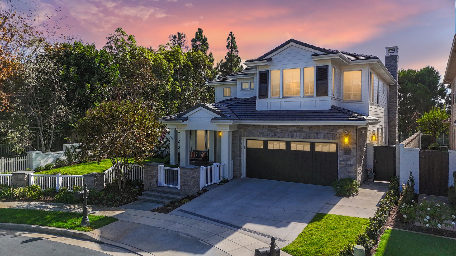 Two-story house with a gray facade, black garage door, and a driveway at dusk.