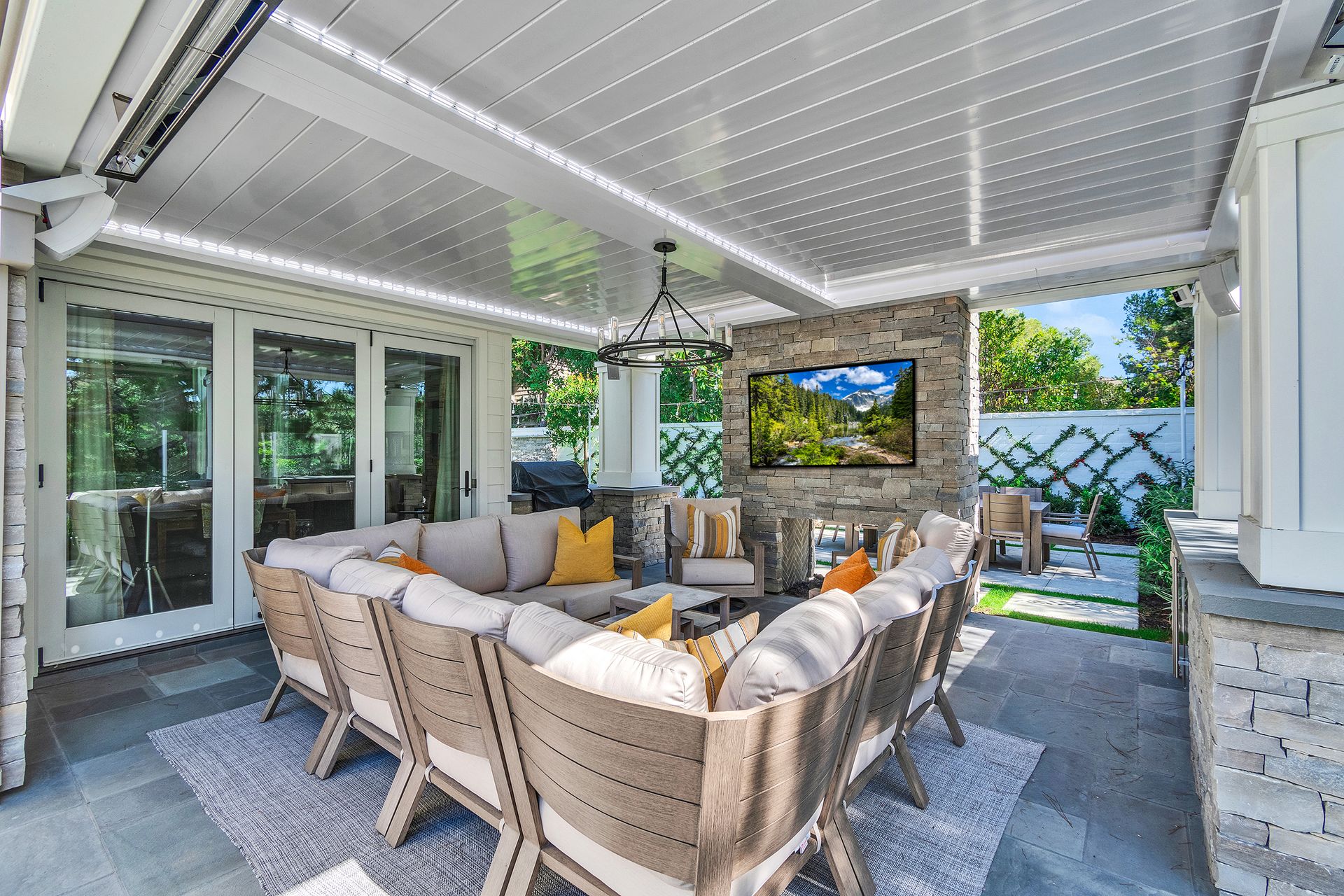 Outdoor patio with sectional seating, fireplace, TV, and overhead lighting.