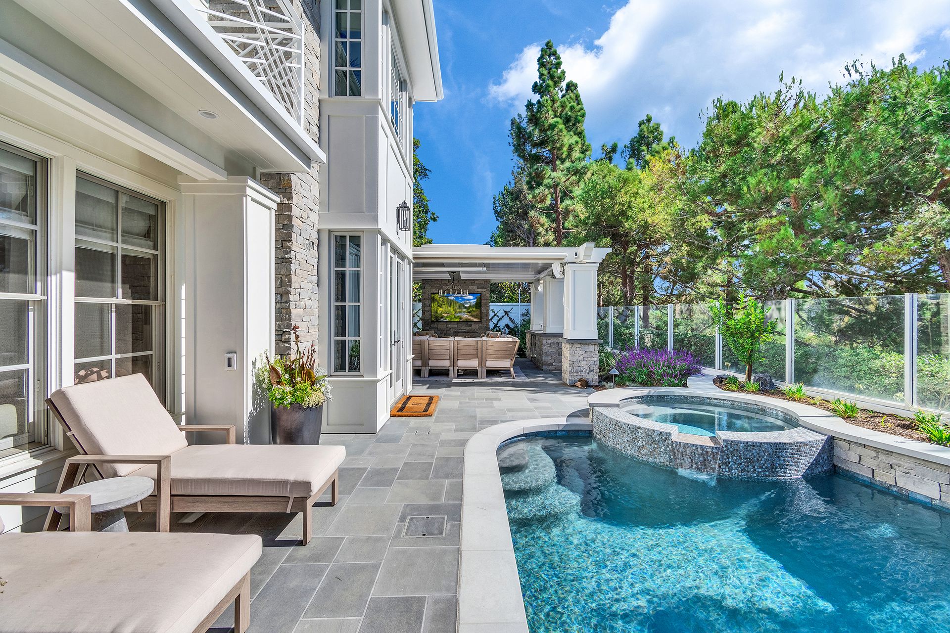 Luxury backyard with pool, patio, and lounge chairs next to a multi-story home on a sunny day.