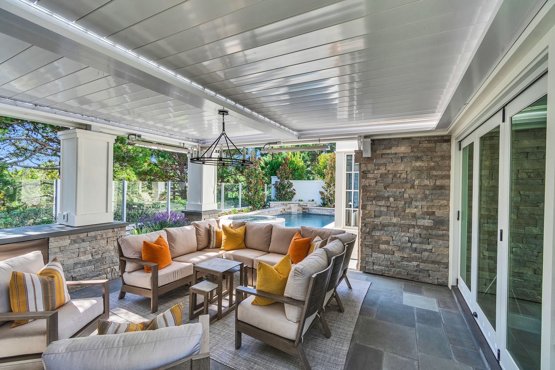Outdoor patio with sectional sofa and stone wall, overlooking a pool.