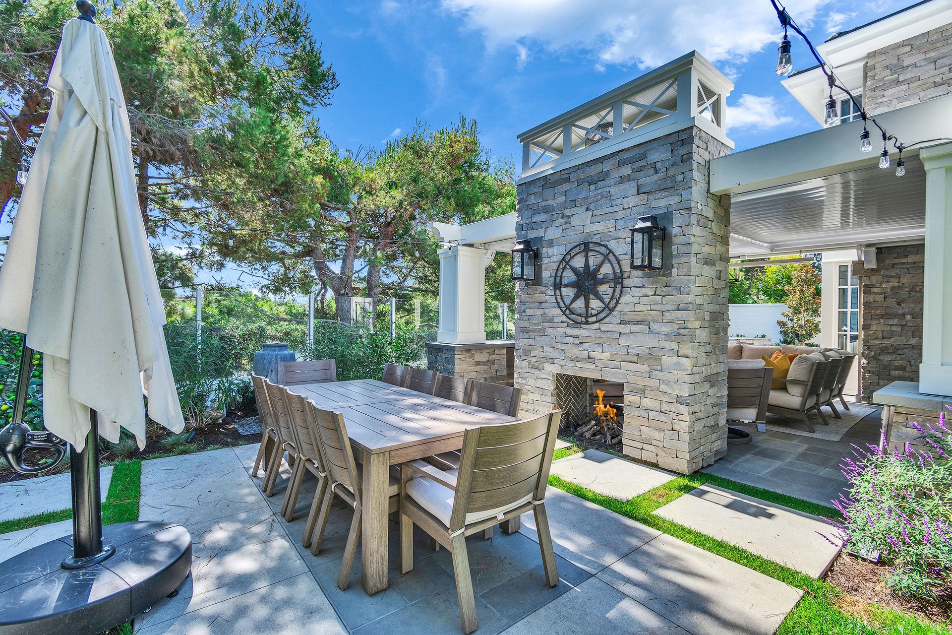 Outdoor patio with dining table, fireplace, and umbrella on a sunny day.