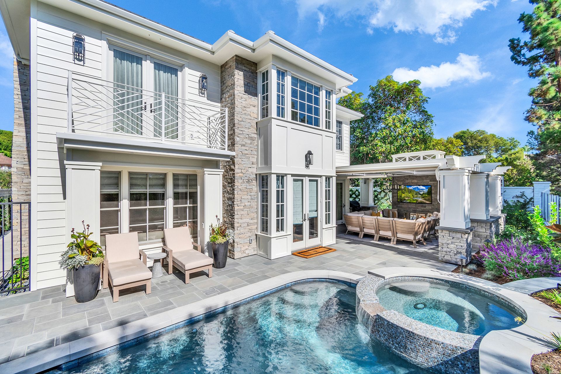 Luxury two-story house with pool and outdoor seating area; light-colored stone and white exterior under a blue sky.
