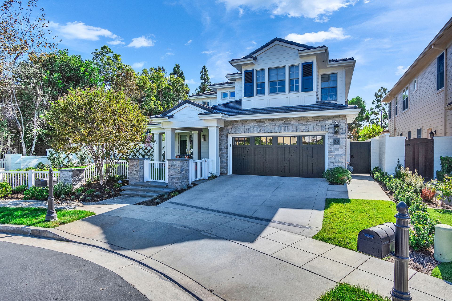 Two-story house with a stone facade, a gray garage door, and a driveway on a sunny day.
