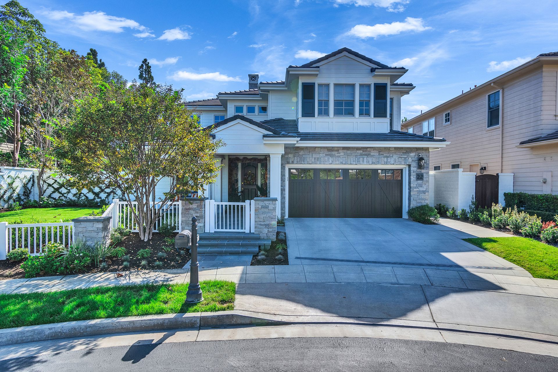 Two-story house with stone accents, garage, driveway, and manicured lawn on a sunny day.