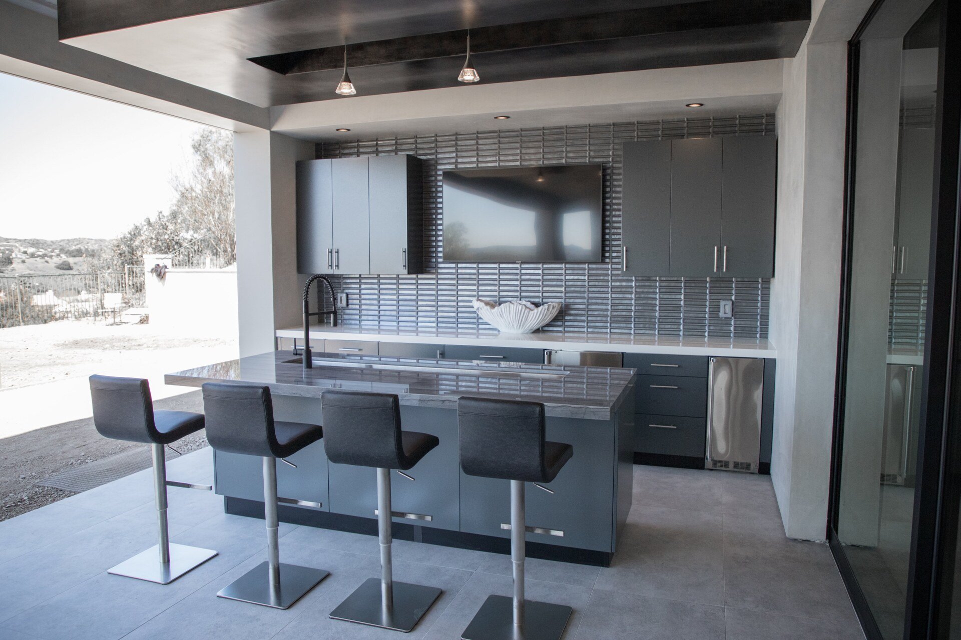 A kitchen with a large island and stools and a flat screen tv on the wall.