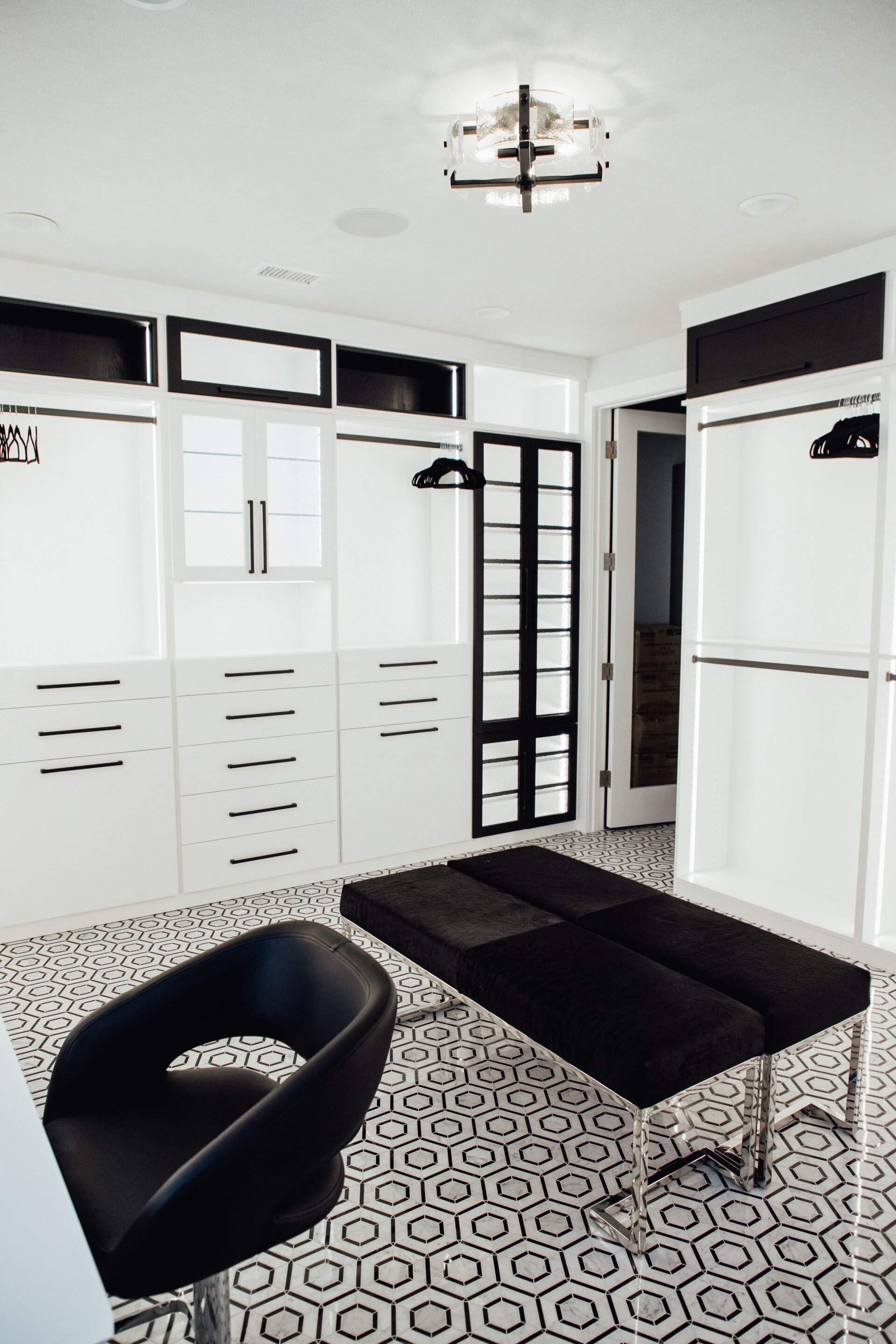 A black and white walk in closet with a black chair and a bench.