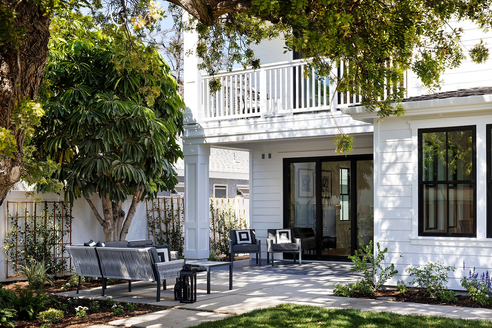 A white house with black windows and a patio with a bench and chairs.