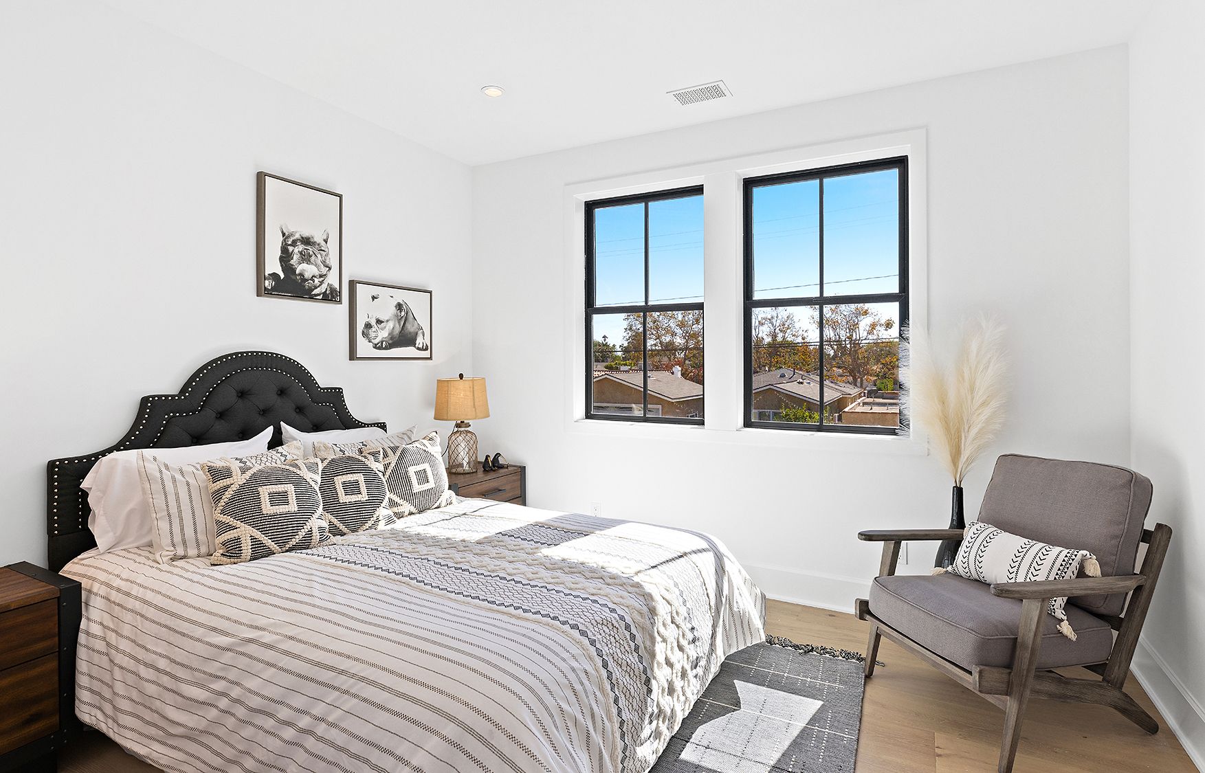 A bedroom with a bed , chair , nightstand and two windows.
